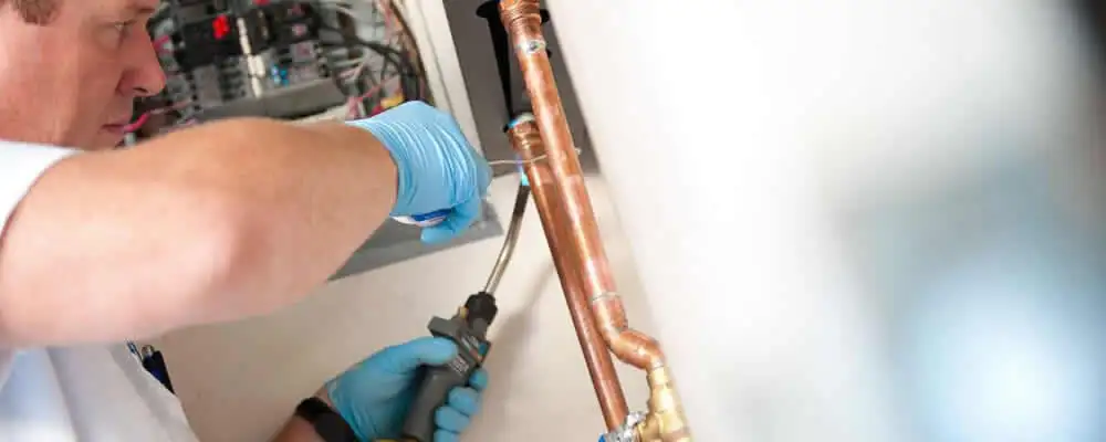 Water heater repair technician testing copper pipe connections and controls in Knoxville, TN